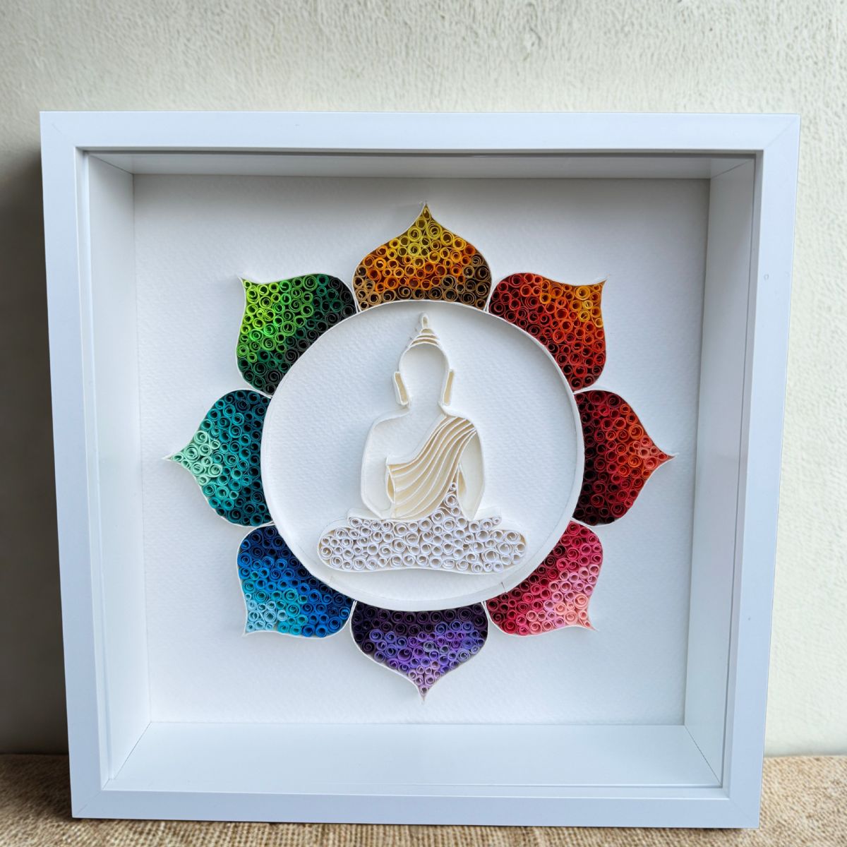 Handcrafted Radiant Lotus Buddha paper quilling wall art featuring a white Buddha silhouette surrounded by a vibrant rainbow lotus in a white shadow box frame.