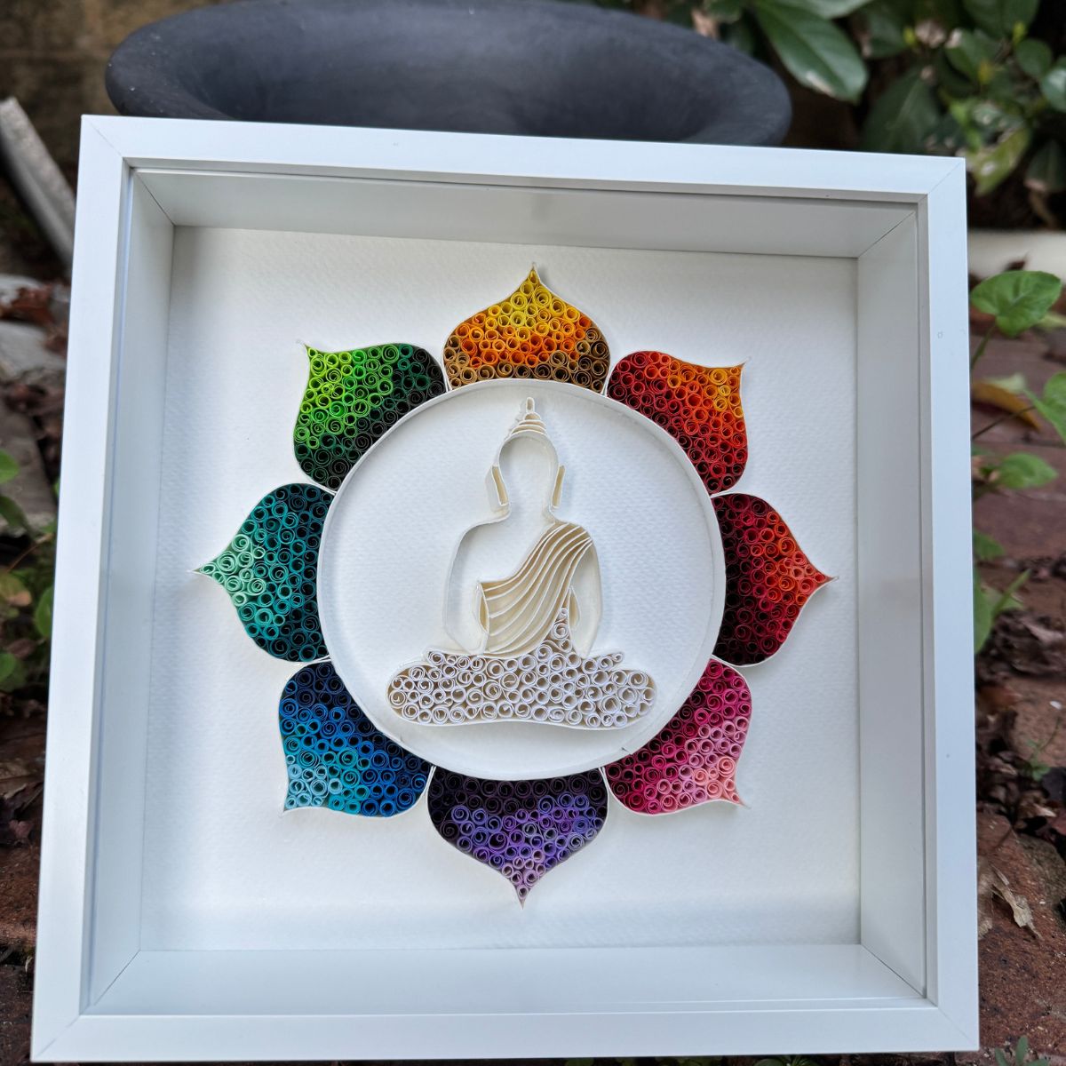 Handcrafted Radiant Lotus Buddha paper quilling wall art featuring a white Buddha silhouette surrounded by a vibrant rainbow lotus in a white shadow box frame.