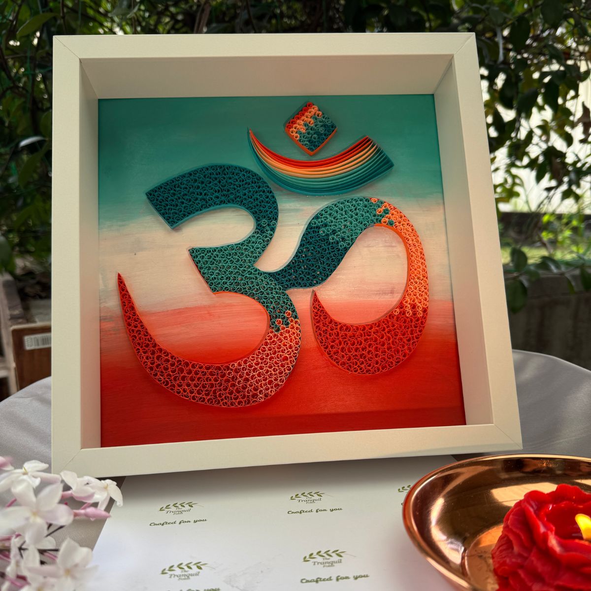 Handcrafted spiritual OM paper quilling artwork in teal, aqua, coral and warm orange tones, framed in white MDF