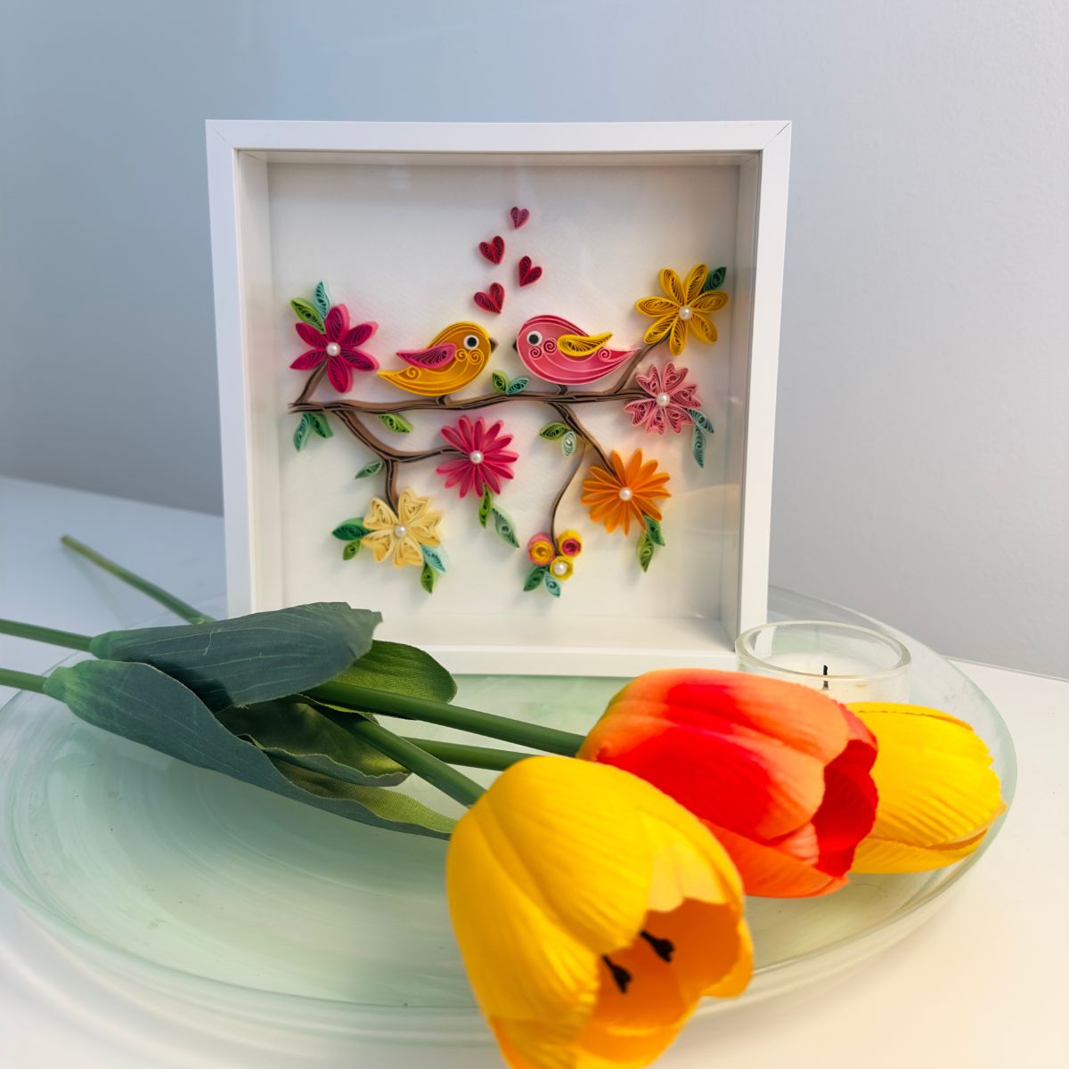 Handcrafted paper quilling artwork featuring two colourful birds perched on a flowering branch surrounded by blooming flowers and heart accents, available framed or unframed.
