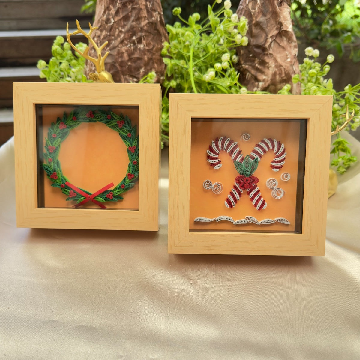 Christmas wreath and candy cane paper quilling artworks in matching light wood-look miniature frames, displayed together on a table.