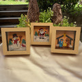 Three miniature paper quilling artworks featuring a snowman, Santa and a nativity scene in matching light wood-look frames, arranged on a table.