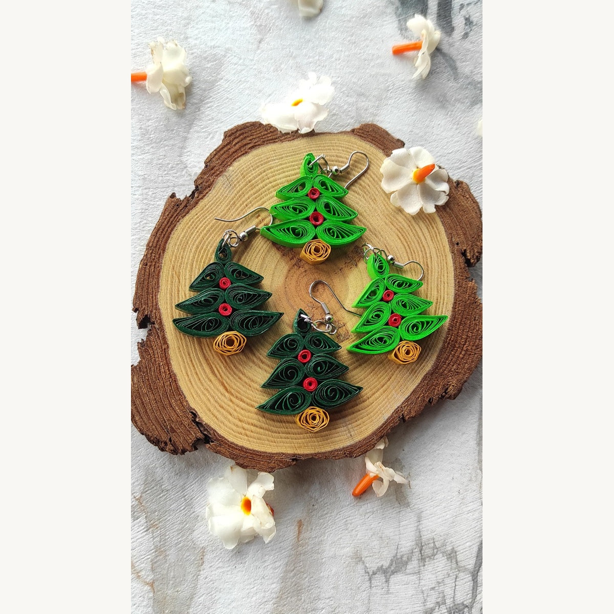 Handmade dark and light green Christmas tree paper quilling earrings with red decorations, golden-yellow bases and German silver hooks on a wood slice.