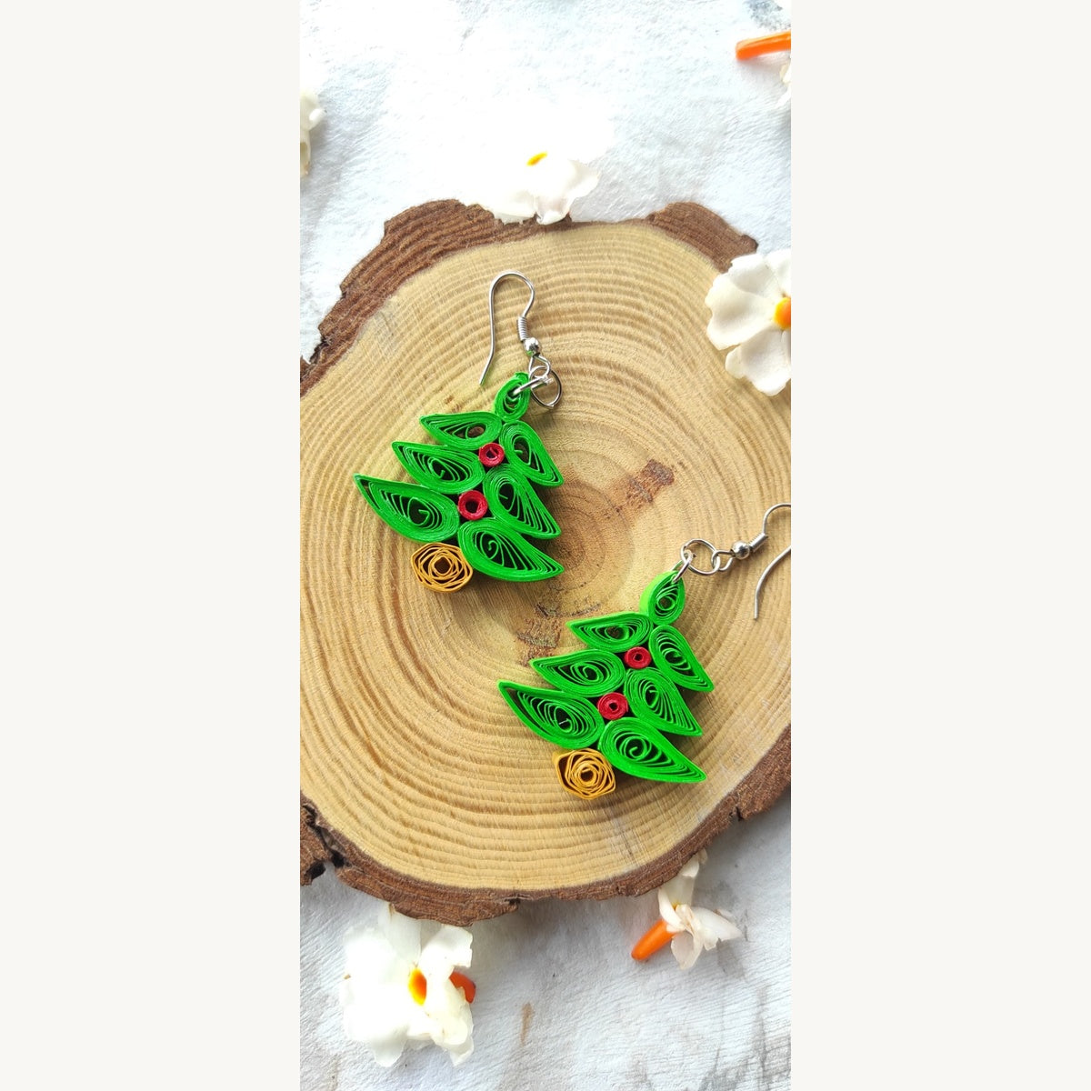 Handmade light green Christmas tree paper quilling earrings with red decorations, golden-yellow bases and German silver hooks on a wood slice.