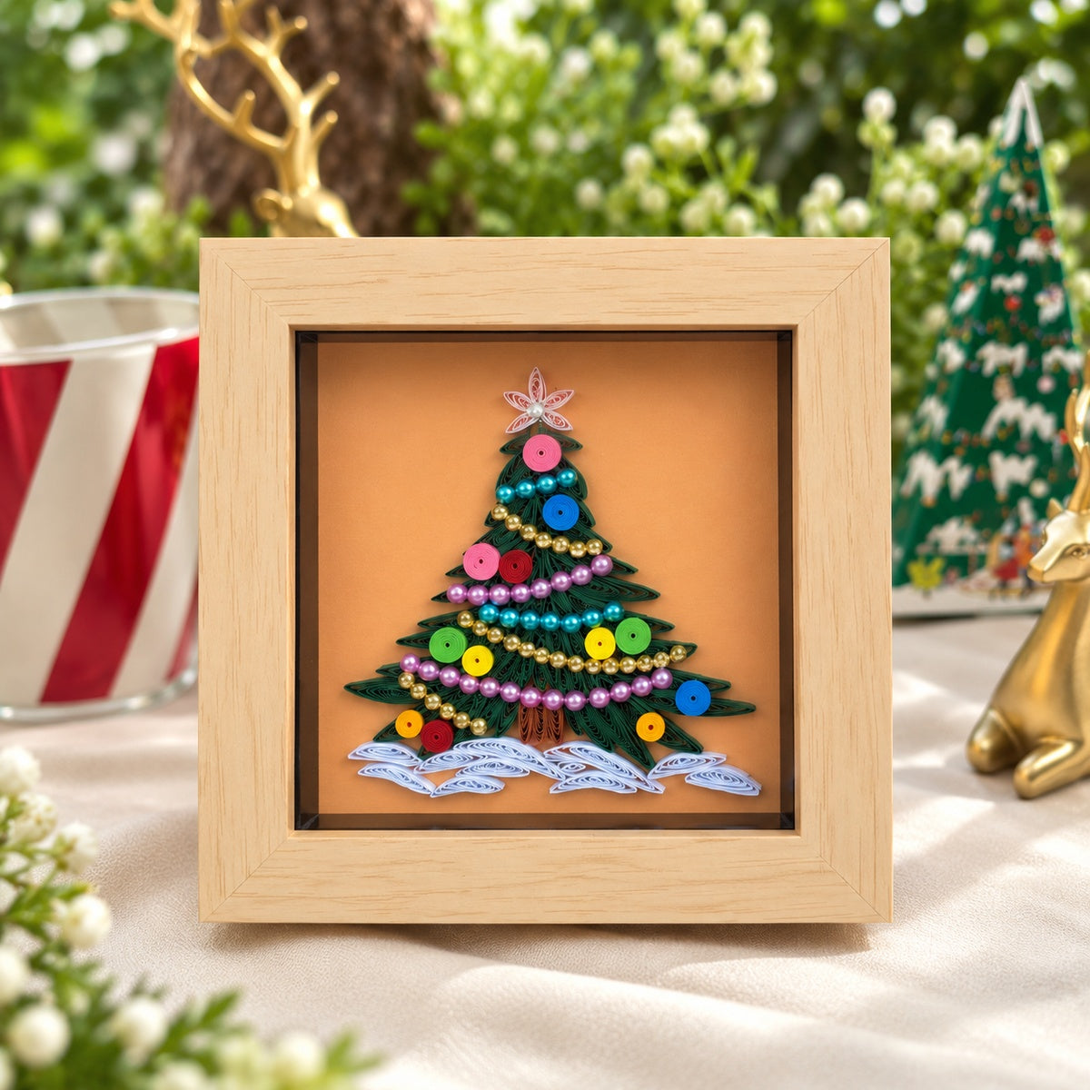 Framed Christmas tree paper quilling artwork with dark green branches, colourful ornaments and bead garlands against a peach background.