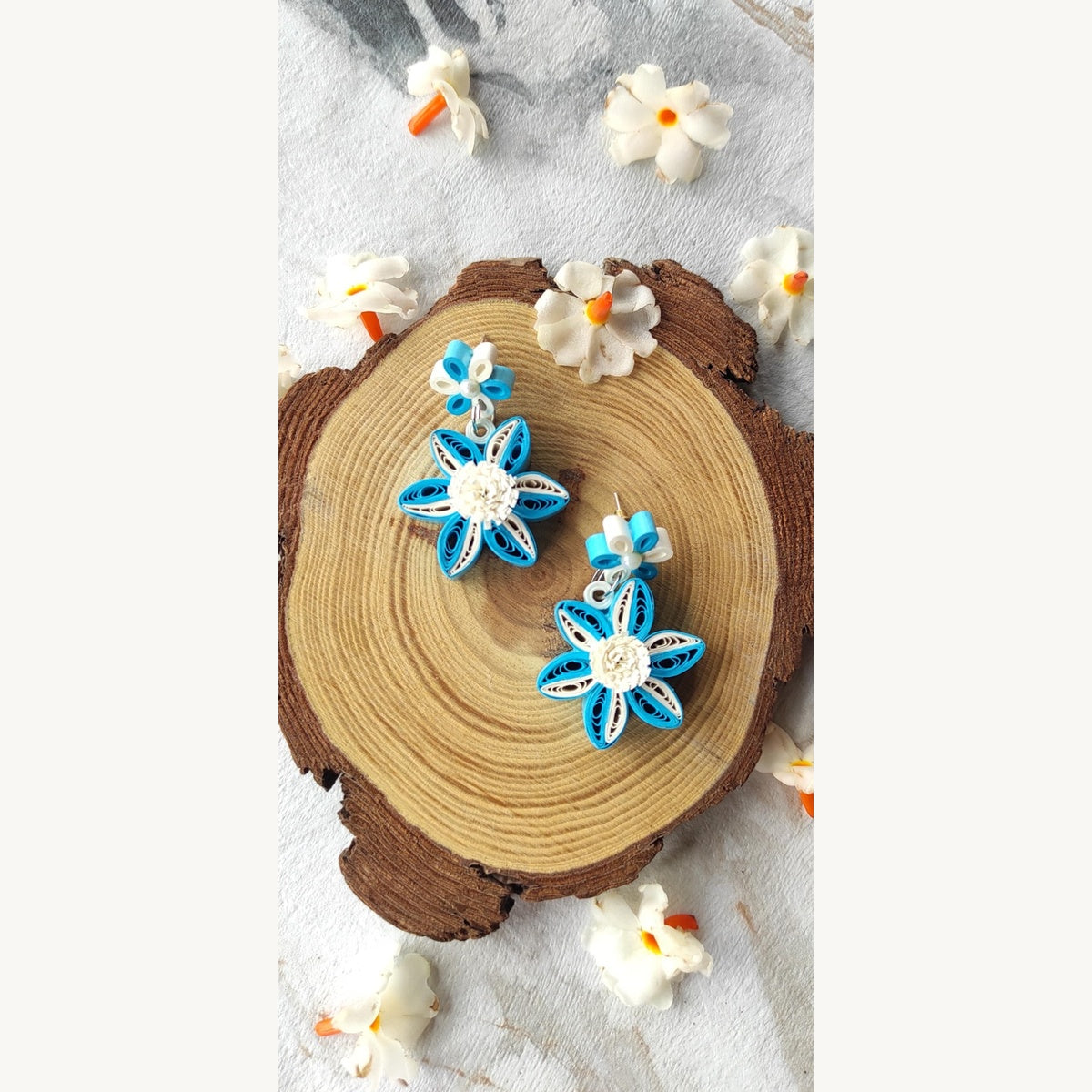Handcrafted blue and white paper quilling flower stud drop earrings with two-tone petals and pearl-look accents.