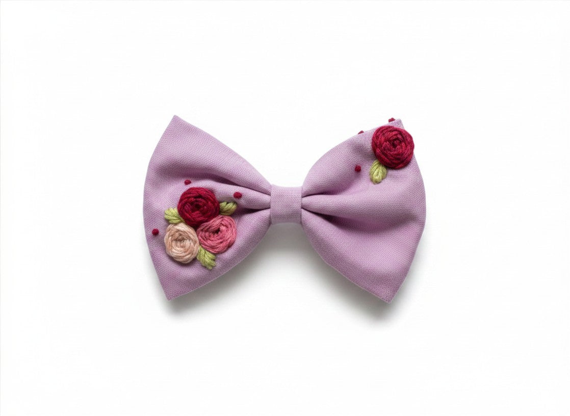 Close-up of hand embroidered three-dimensional rose cluster on lavender cotton bow — crimson deep pink and blush artisan stitching