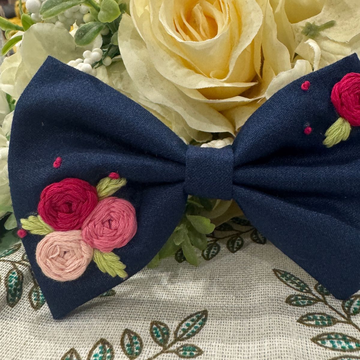 A navy blue fabric hair bow with embroidered pink and red roses, green leaves, and small pink dots