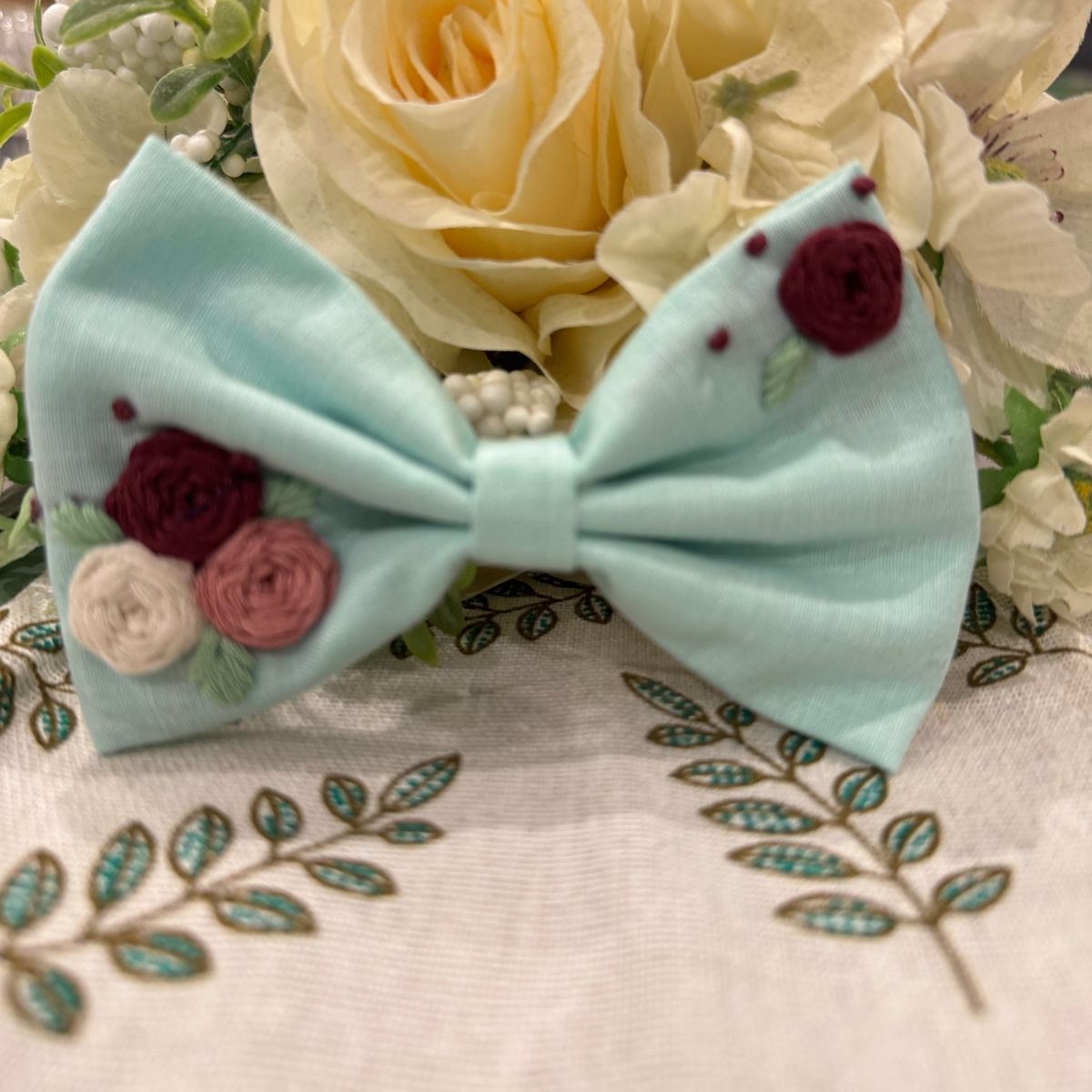 A light blue fabric hair bow decorated with embroidered red, pink, and cream flowers