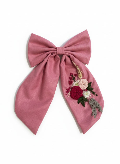 Hand embroidered floral pigtail bow in dusty pink cotton fabric featuring artisan floral stitching and alligator clip attachment for girls' hairstyles.