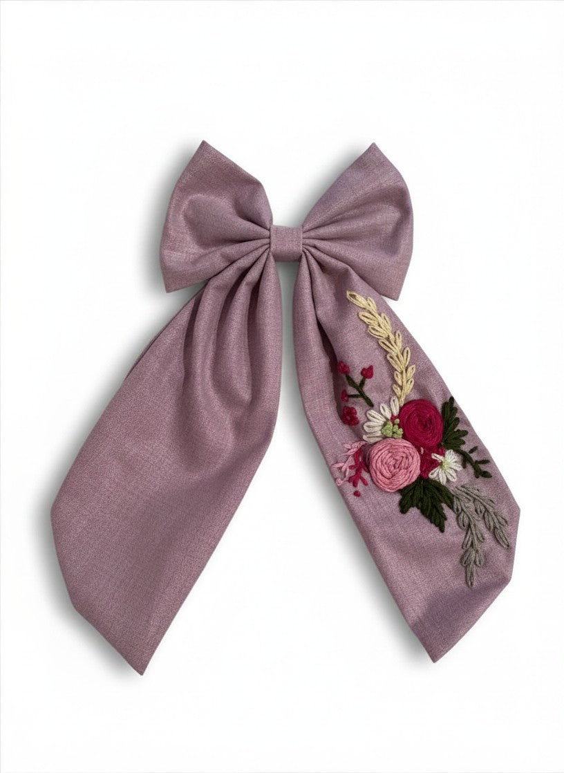 Close-up of hand embroidered mixed floral bouquet on lavender sailor bow tail — crimson pink roses white daisies and green foliage
