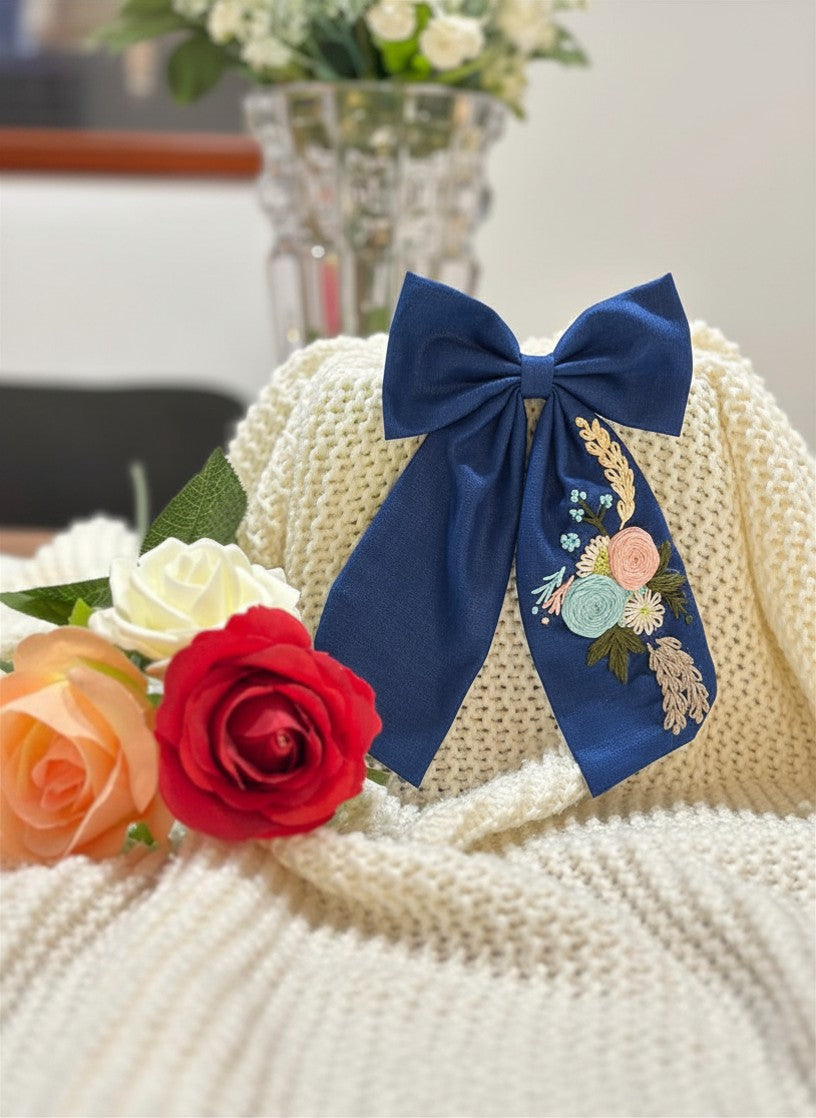 Hand embroidered floral pigtail bow in moonlit bluecotton fabric featuring artisan floral stitching and alligator clip attachment for girls' hairstyles.