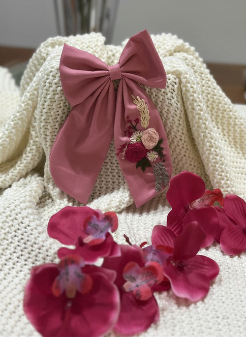 Hand embroidered floral pigtail bow in dusty pink cotton fabric featuring artisan floral stitching and alligator clip attachment for girls' hairstyles.
