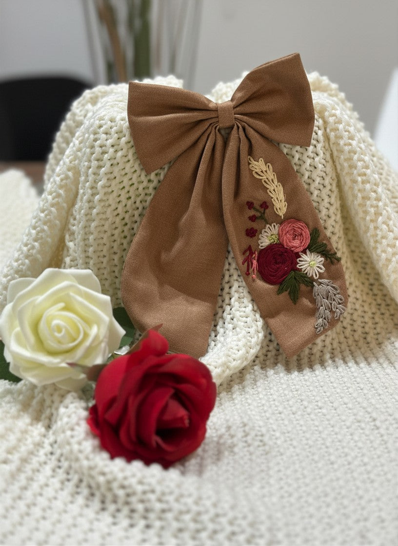 Hand embroidered floral pigtail bow in chestnut brwon cotton fabric featuring artisan floral stitching and alligator clip attachment for girls' hairstyles