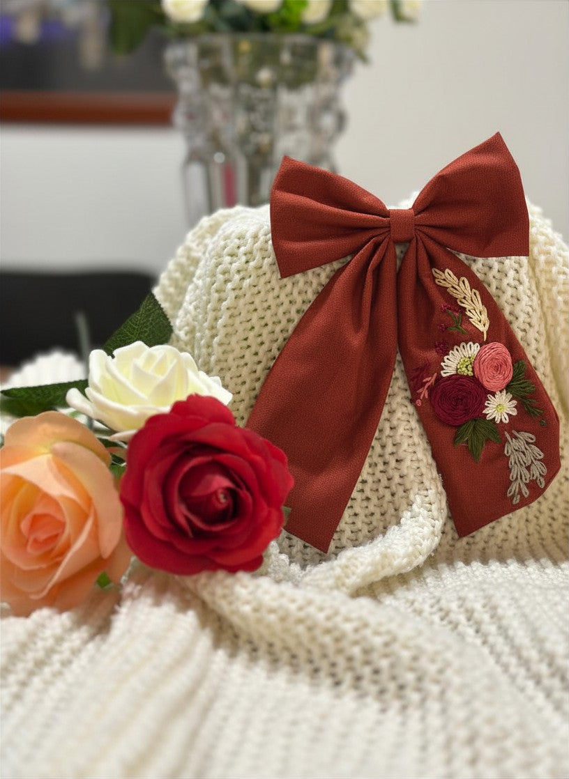 Hand embroidered floral pigtail bow in hazel brown cotton fabric featuring artisan floral stitching and alligator clip attachment for girls' hairstyles.