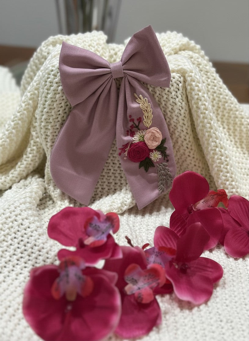 Hand embroidered floral pigtail bow in lavender cotton fabric featuring artisan floral stitching and alligator clip attachment for girls' hairstyles.