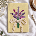 Hand embroidered floral bouquet journal in lemon yellow with purple and magenta embroidery and cream crochet bow styled on white linen.