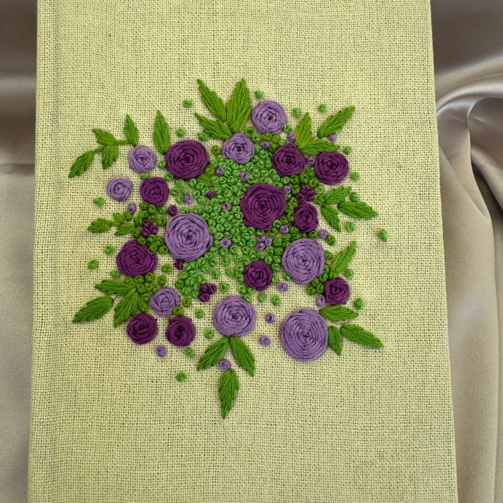 Hand embroidered floral journal with lilac and plum rose bouquet stitched on a pale lemon-yellow linen cover.