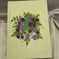 Hand embroidered floral journal with lilac and plum rose bouquet stitched on a pale lemon-yellow hessian cover.