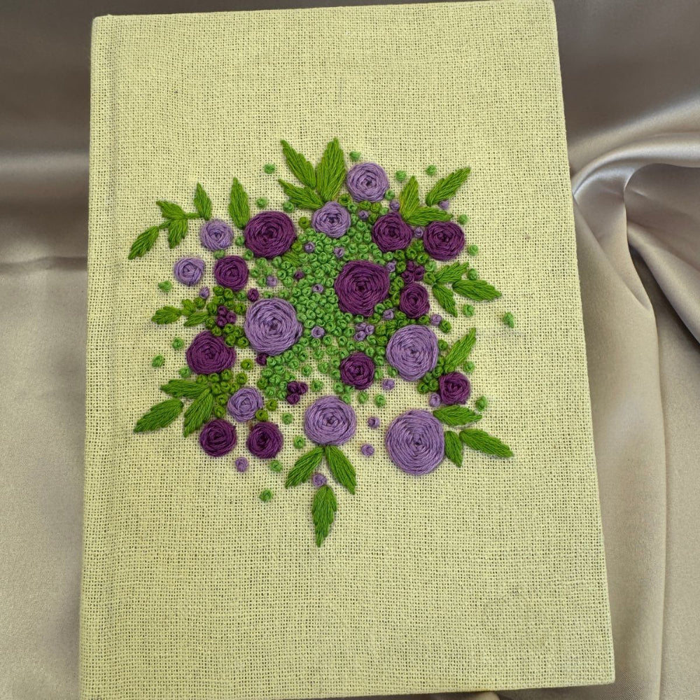 Hand embroidered floral journal with lilac and plum rose bouquet stitched on a pale lemon-yellow hessian cover.