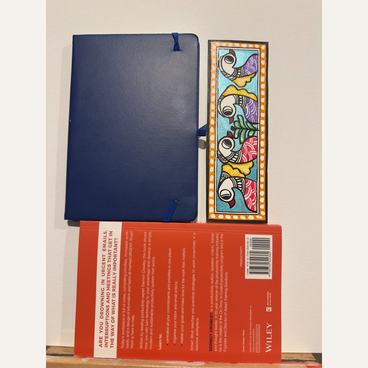 Hand-painted Madhubani bookmark featuring four purple and red birds on a turquoise background with an orange dotted border, beside a navy notebook and book for size reference. Book and notebook not included.