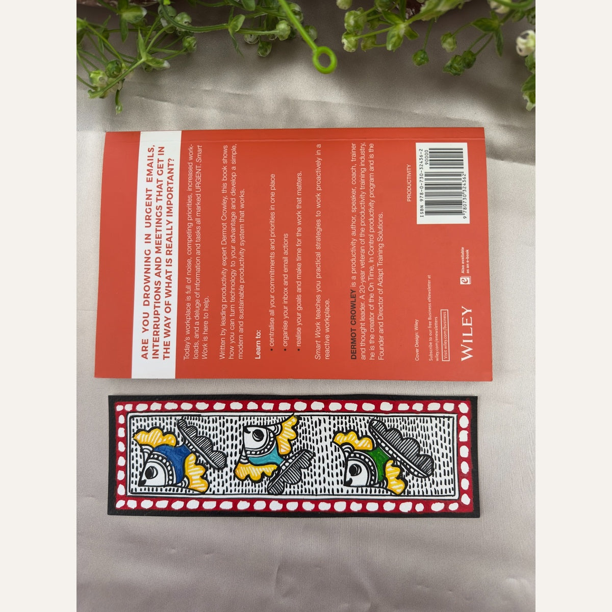 Hand-painted Madhubani Colourful Trio fish bookmark with black-and-white patterns, colourful fish and a deep red border, beside a book for size reference. Book not included.