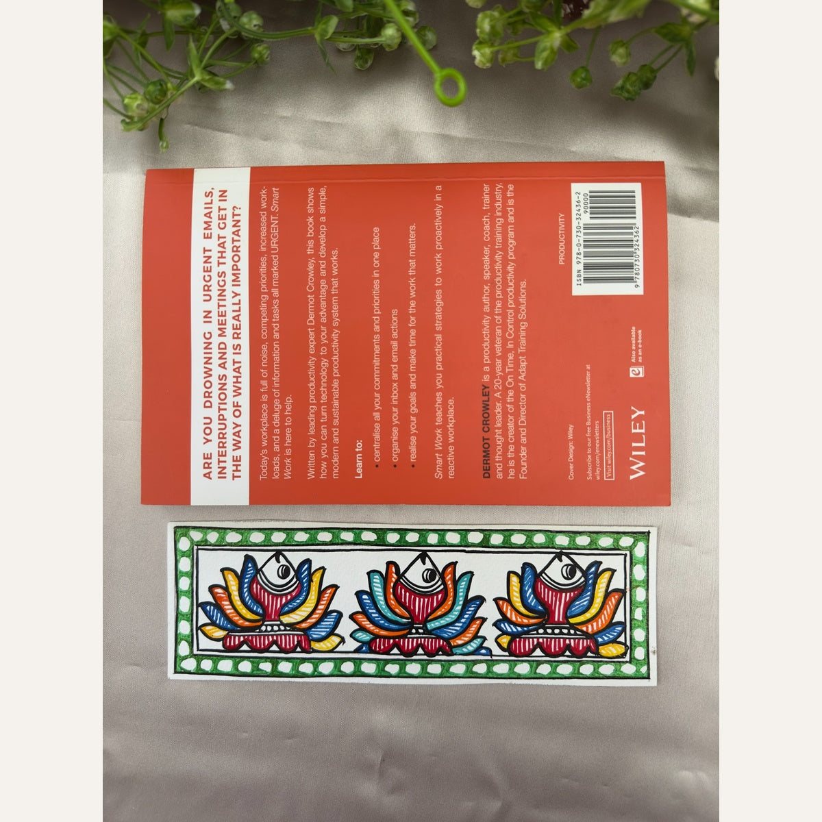 Hand-painted Madhubani Rainbow Fins bookmark featuring three fish with colourful fan-like fins and a green border with white dots, beside a book for size reference. Book not included.