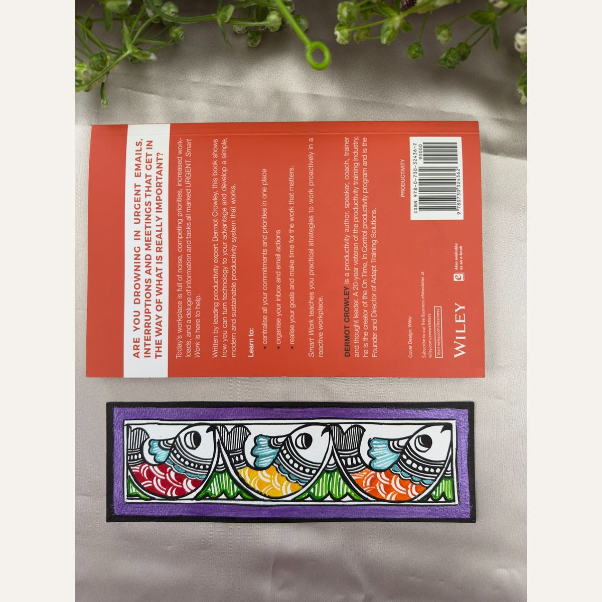 Hand-painted Madhubani Violet Parade bookmark with three red, yellow and orange fish, turquoise accents and a violet-purple border, beside a book for size reference. Book not included.