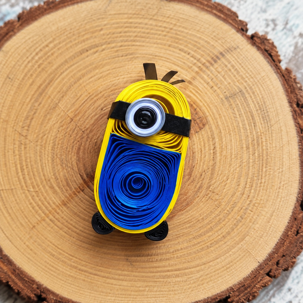 Handcrafted one-eye paper quilling character fridge magnet displayed on a natural wood slice.
