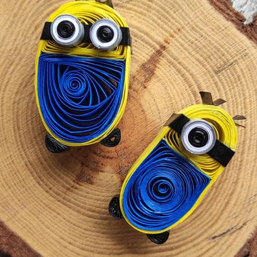 One-eye and two-eye handcrafted paper quilling character fridge magnets displayed together on a natural wood slice.