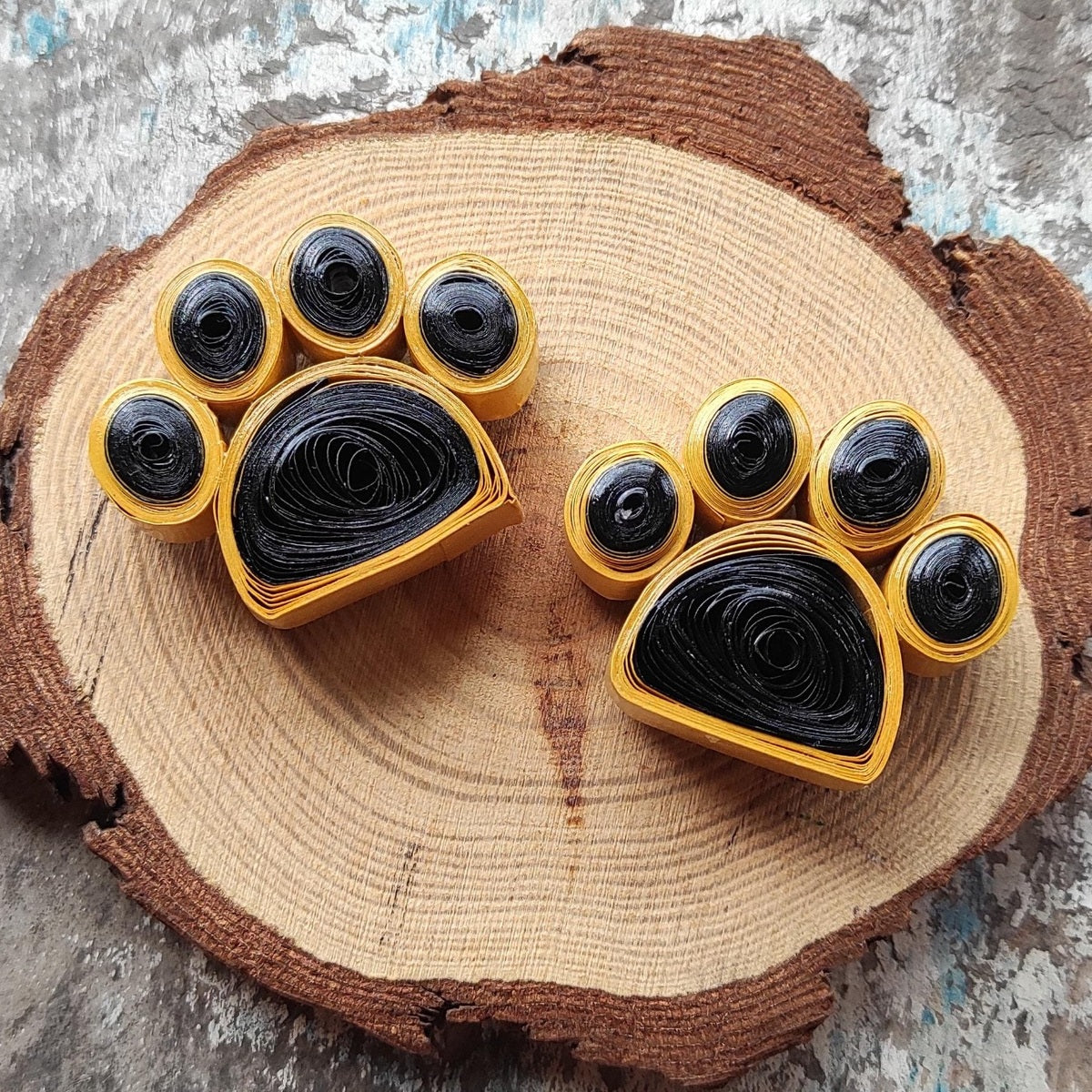 Handmade black and gold paper quilling paw fridge magnets displayed on a natural wood slice.