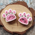 Handmade pink and white paper quilling paw fridge magnets displayed on a natural wood slice.