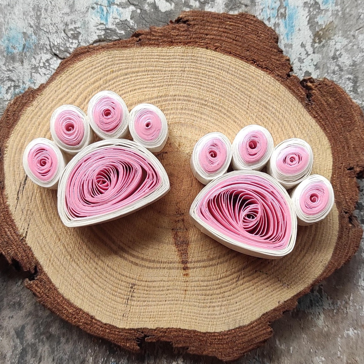 Handmade pink and white paper quilling paw fridge magnets displayed on a natural wood slice.