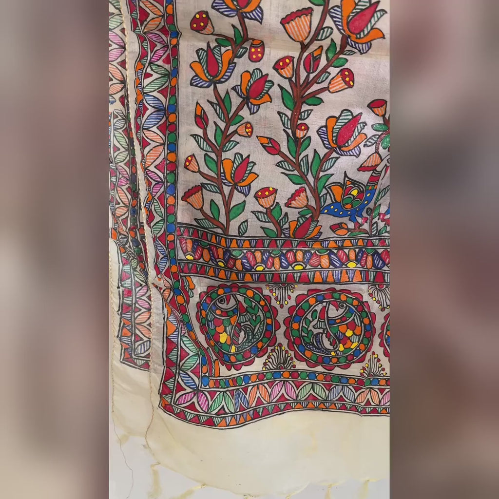 Close-up video of an ivory cream hand-painted Madhubani art silk stole featuring colourful peacock, floral and fish motifs with intricate decorative borders.