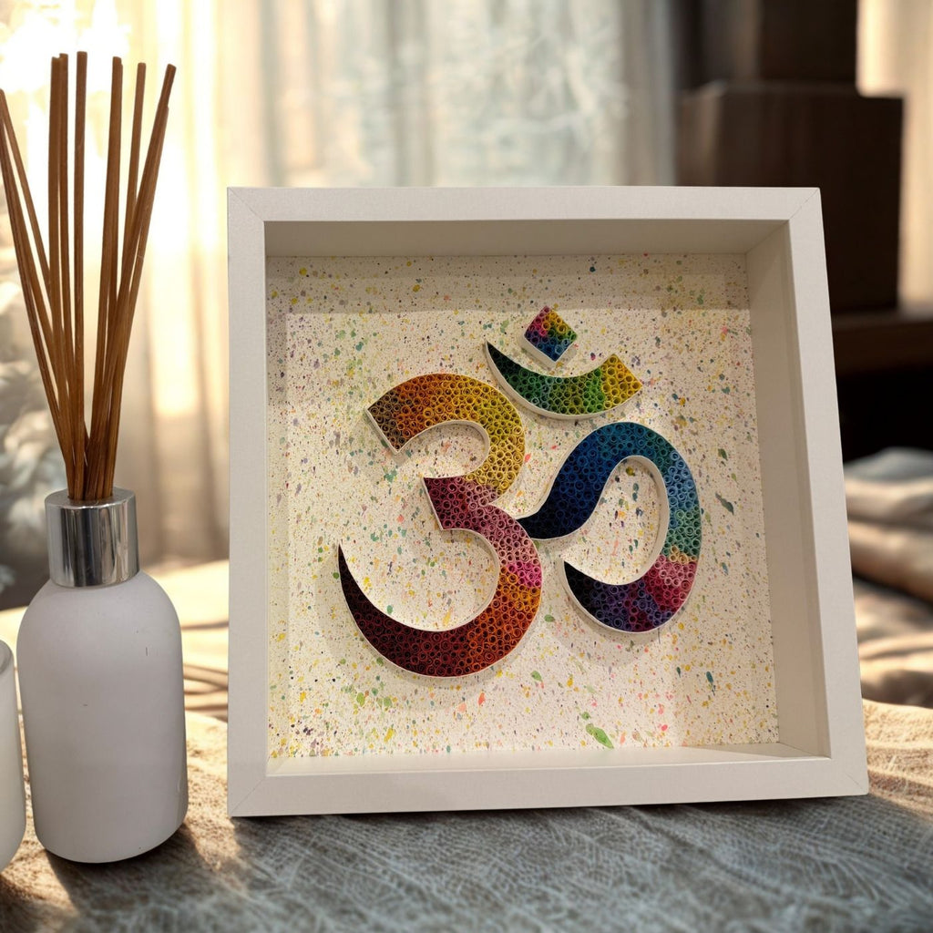 Handcrafted rainbow Om paper quilling artwork in a white shadow box frame featuring intricate paper coils on a hand-painted splatter background, ideal for meditation and spiritual home décor.
