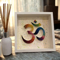 Handcrafted rainbow Om paper quilling artwork in a white shadow box frame featuring intricate paper coils on a hand-painted splatter background, ideal for meditation and spiritual home décor.