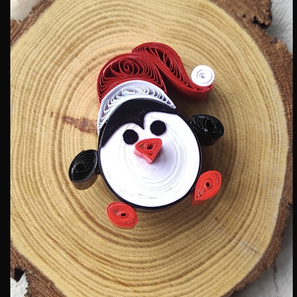 Handmade red, white and black Santa paper quilling fridge magnet displayed on a natural wood slice.